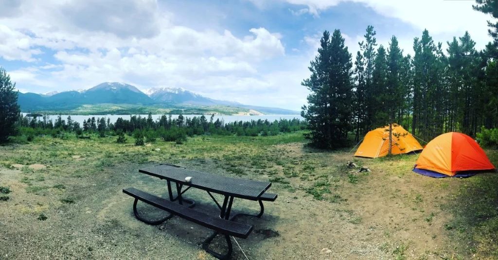 Outdoor adventure in Colorado showing safe camping preparation with gear, campfire area, and forest campsite.
